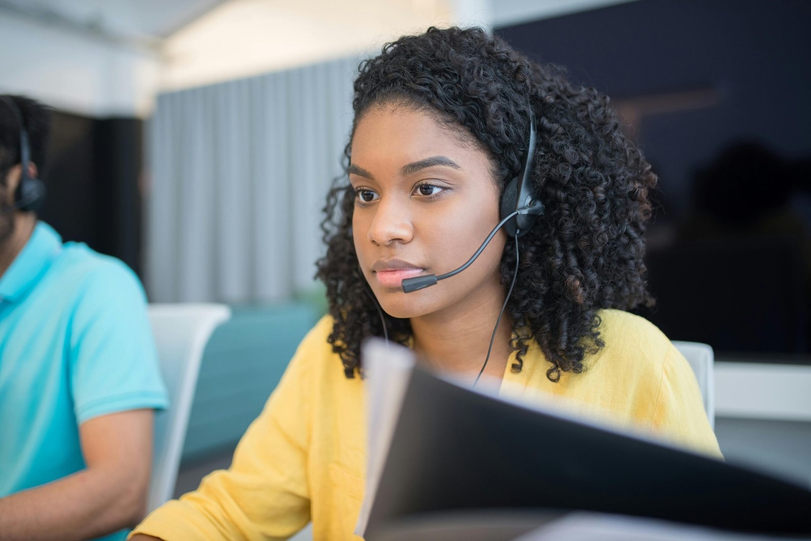 A professional call center agent wearing a headset, working indoors with focused attention.